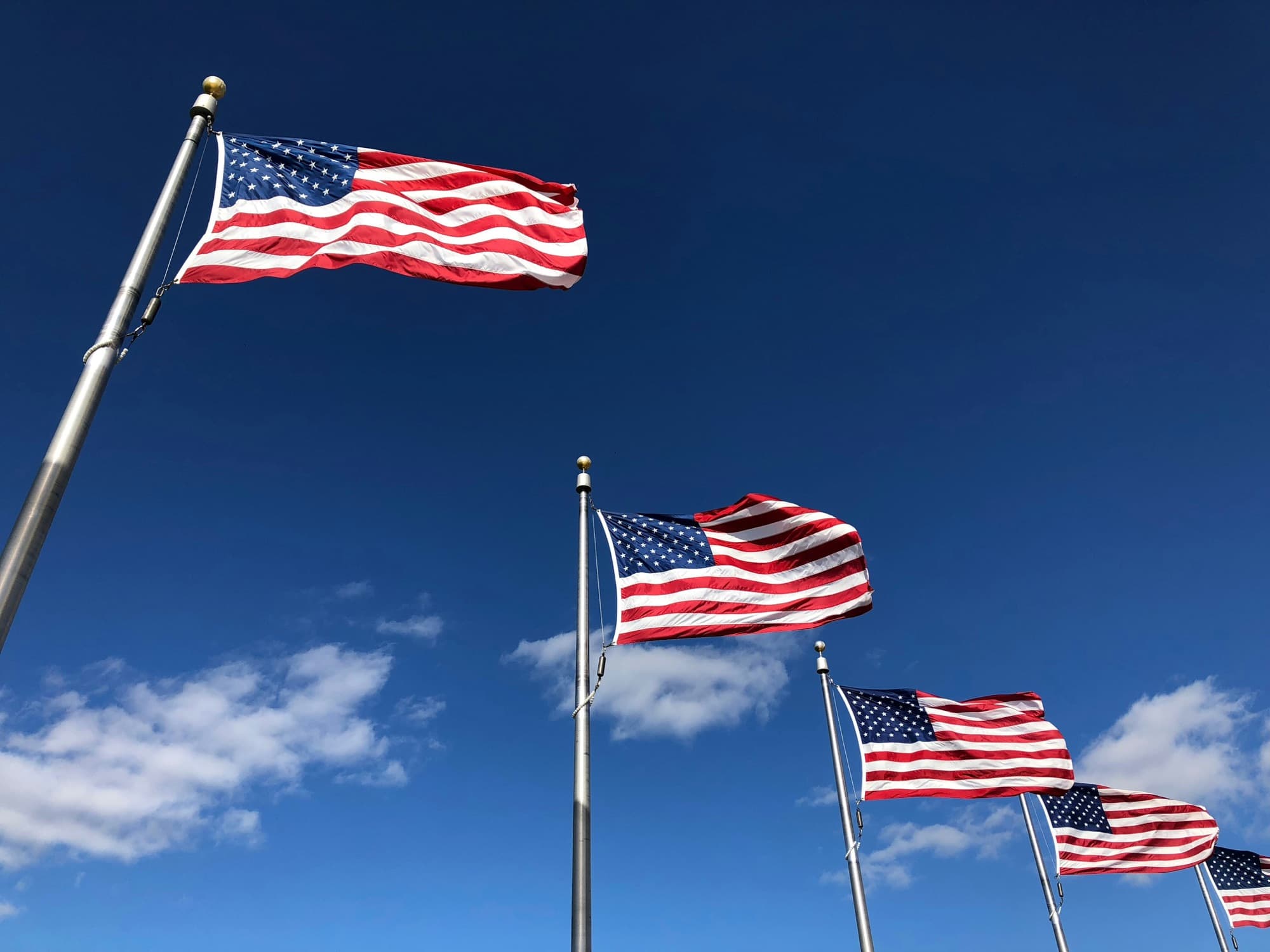 Four United States flags flying against a blue sky