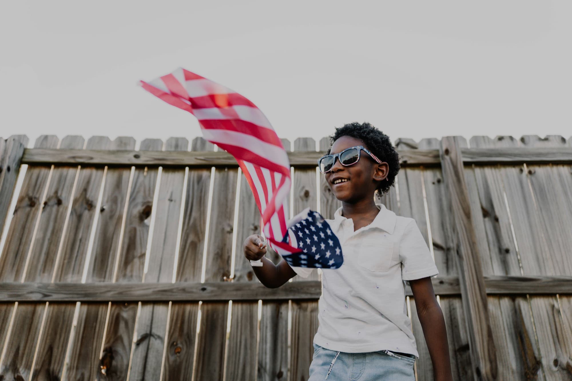 A child waving a small United States flag in a backyard